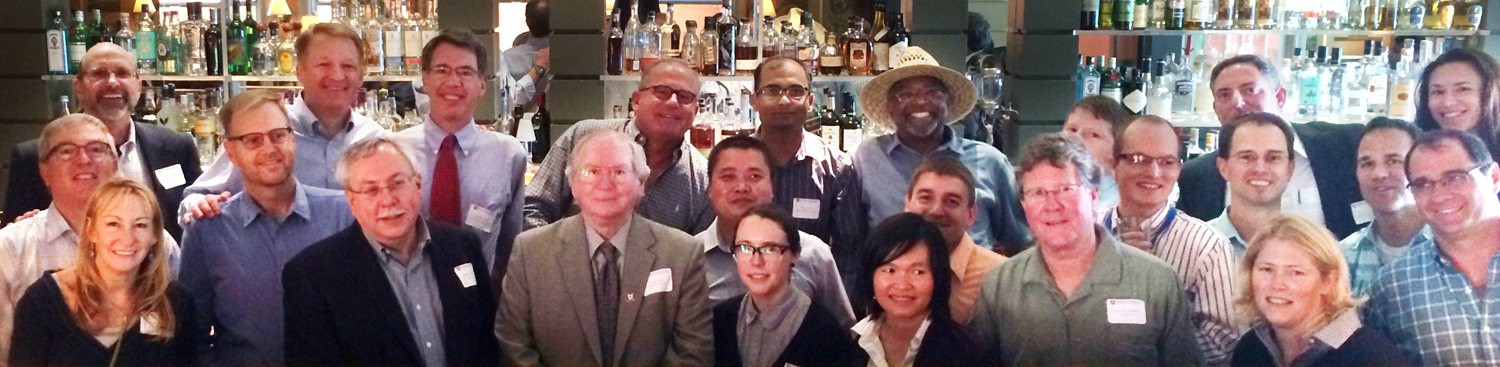 Inside a bar, a large gathering of alumni from the Keck Group smile at the camera